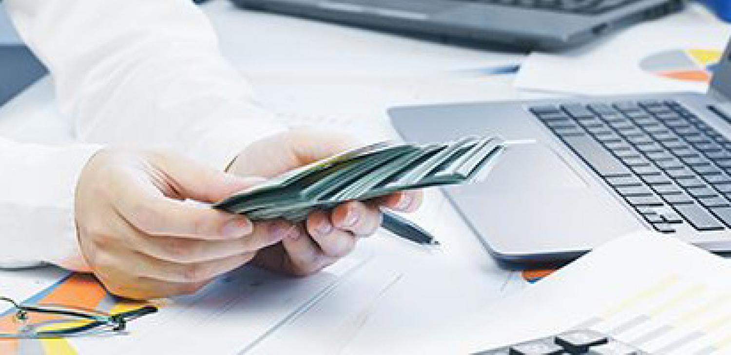 business man counting cash at desk with computer