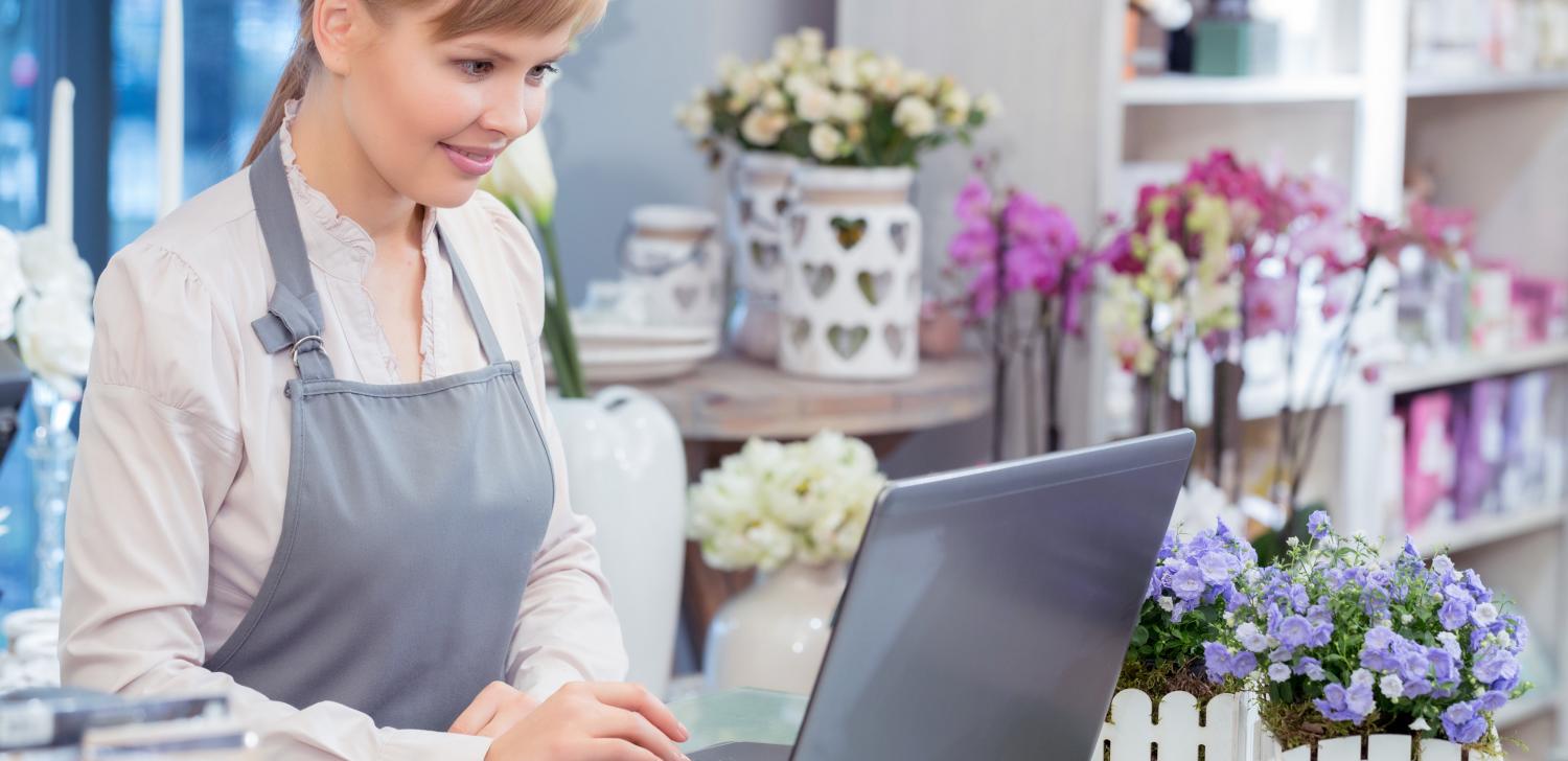 Woman with apron uses laptop at floral shop
