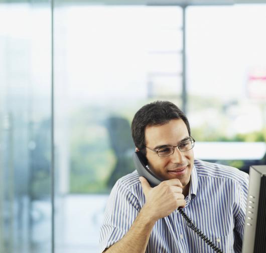 Man in Office Looking at Computer and Talking on Phone Thumbnail